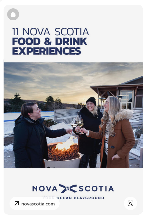 Three people standing outside around a fire in wintertime and holding up glasses of wine to cheers.