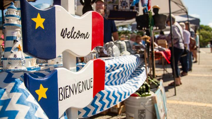 Two blue, white and read Acadian flag welcome signs in English and French located on a outdoor market kiosk